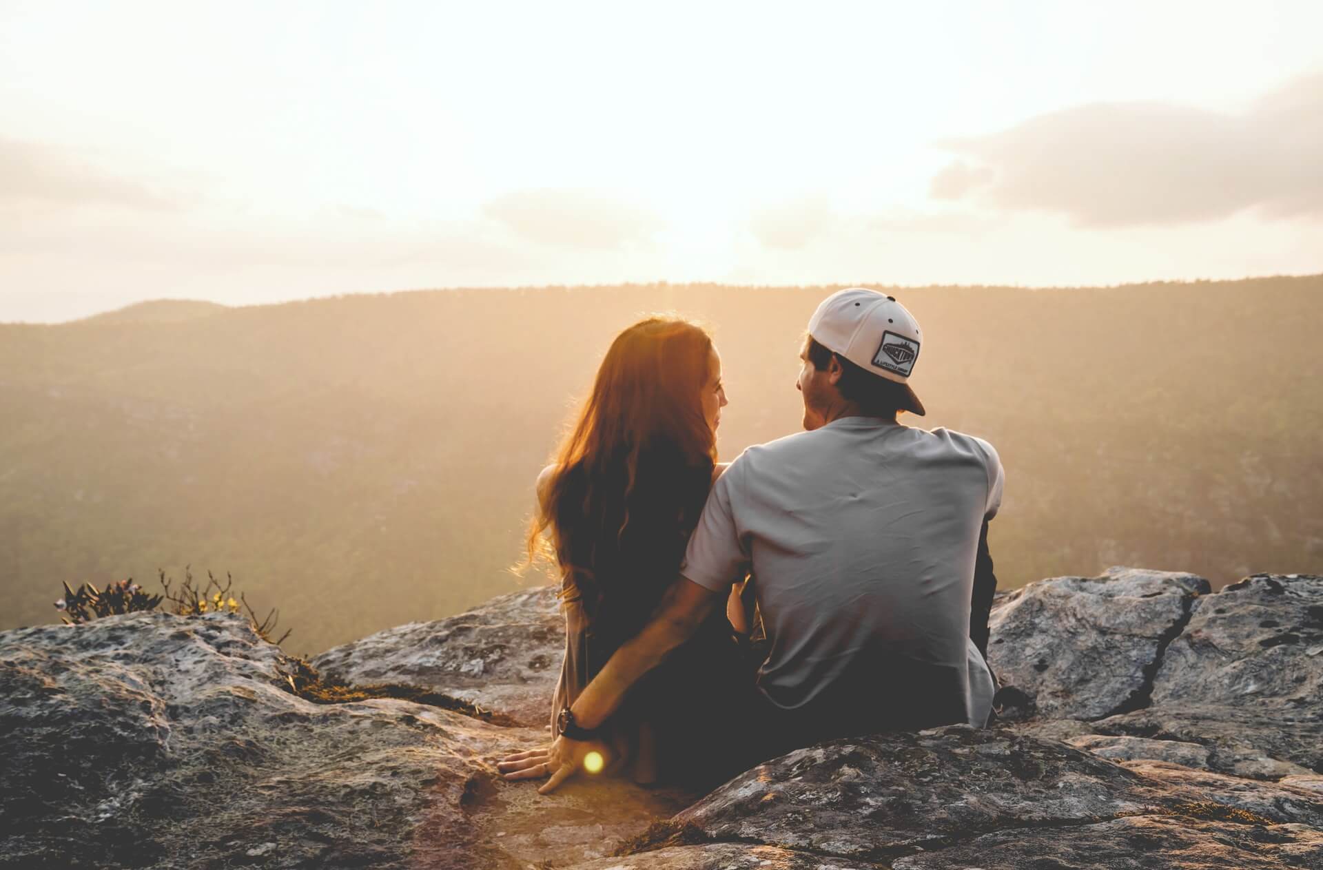 Couple sitting on rocky cliff at sunset, ideal for engagement videos Tampa and affordable wedding videography.