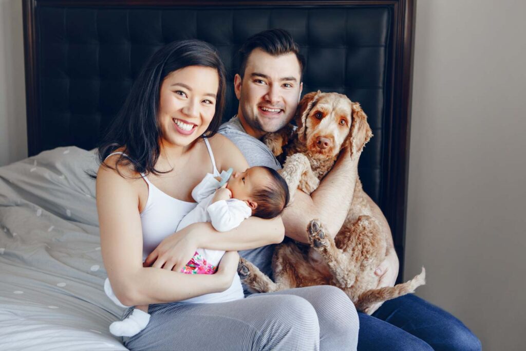 Family with newborn and dog on bed, smiling. Tampa family videography, engagement videos, affordable wedding videos.